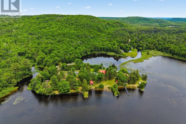 Aerial view of buildings on a peninsula jutting into a dark lake, with forested hills in the background. - 1282 Carroll Road, Dysart Et Al