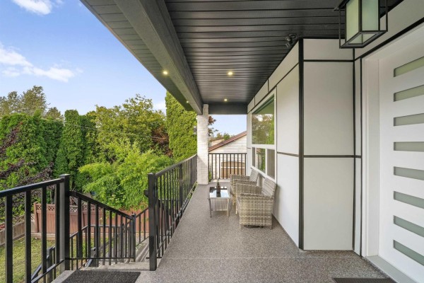 Covered front porch with seating area, modern white siding, and black railings. - 12822 114a Avenue, Surrey
