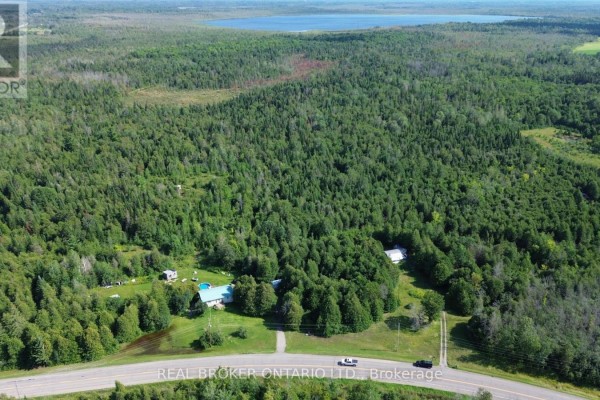 Aerial view of the wooded property with distant water body and scattered residential structures. - 12830 County  15 Road, Merrickville Wolford