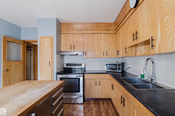 Kitchen with light wood cabinets, black countertops, and a stainless steel sink and faucet. - 12831 126 St Nw, Edmonton