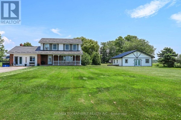 Front view of a two-story house with a white exterior, red brick foundation, and a large covered porch. - 1284 Cheapside Road, Haldimand