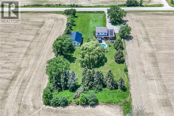 Aerial view of a farmhouse and outbuilding nestled amongst mature trees, surrounded by harvested agricultural fields. - 1284 Cheapside Road, Jarvis