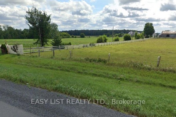 View of a long white fence running along a green field with trees and farm buildings in the distance. - 12860 County  Road 43, North Dundas