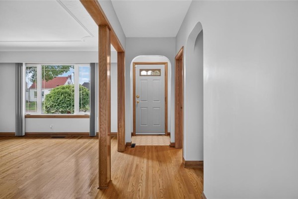 Interior hallway view with a white front door, archway, and hardwood floors. - 1287 Strathcona Street, Winnipeg