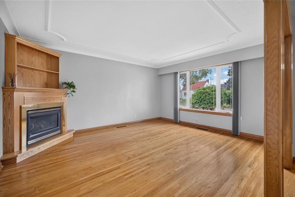 Living room with a gas fireplace, built-in wooden bookshelf, and large window. - 1287 Strathcona Street, Winnipeg