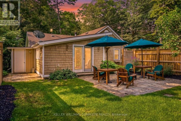 Backyard patio with wooden tables, chairs, and teal umbrellas adjacent to the house at dusk. - 1288 Walker Lane, Fort Erie