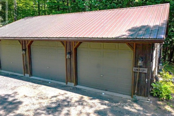 Three-car garage with tan doors, wooden trim, metal roof, and a sign that says 'LAKE'. - 1289 Delbrooke Road S, Lake Of Bays