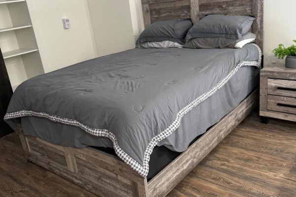 Bedroom with a queen-size bed, grey bedding, wood headboard, and nightstand with plant. - 129 - 135 Station Street, Belleville