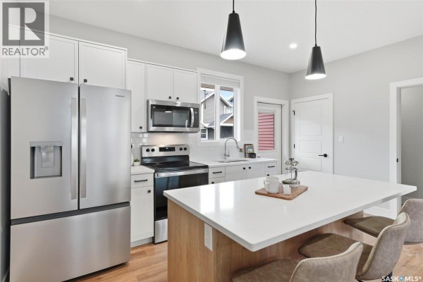 Bright kitchen featuring a stainless steel refrigerator, island with bar seating, and white countertops. - 129 3220 11th Street W, Saskatoon