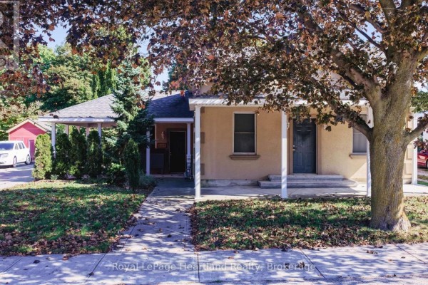 Front view of a light brown stucco house with two entrances, visible trees and sidewalk. - 129 Bayfield Road, Goderich)