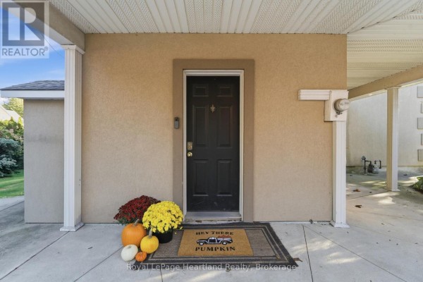 Front door of a stucco house with a doormat and autumn decorations, under a covered porch. - 129 Bayfield Road, Goderich)