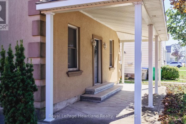 Side entrance to a stucco house with concrete steps and a white covered porch. - 129 Bayfield Road, Goderich)
