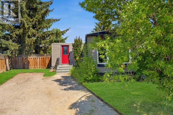 Front view of the mobile home with a gravel driveway and green lawn. - 129 Big Hill Place Se, Airdrie