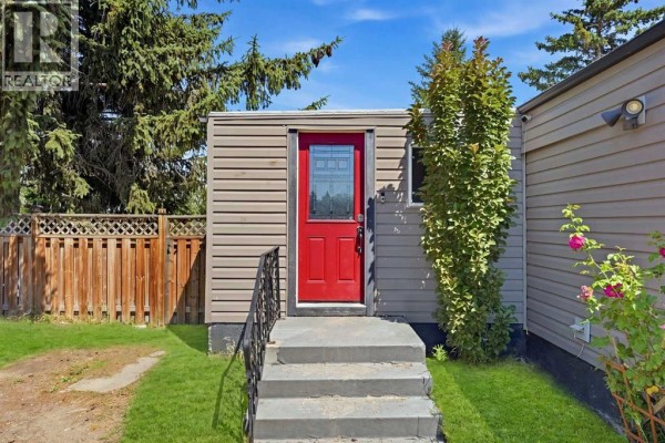 Close-up of the gray siding, red front door, and concrete steps of the mobile home. - 129 Big Hill Place Se, Airdrie