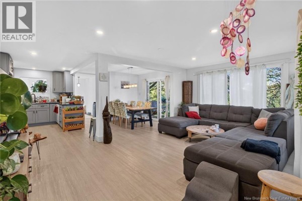 Open concept living area with grey sectional sofa, kitchen with grey cabinets, dining table. - 129 Gaskin, Riverview