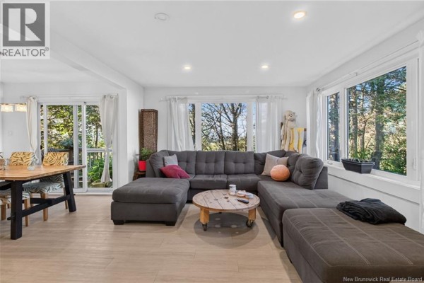 Living room with large grey sectional sofa, coffee table, and windows overlooking trees. - 129 Gaskin, Riverview