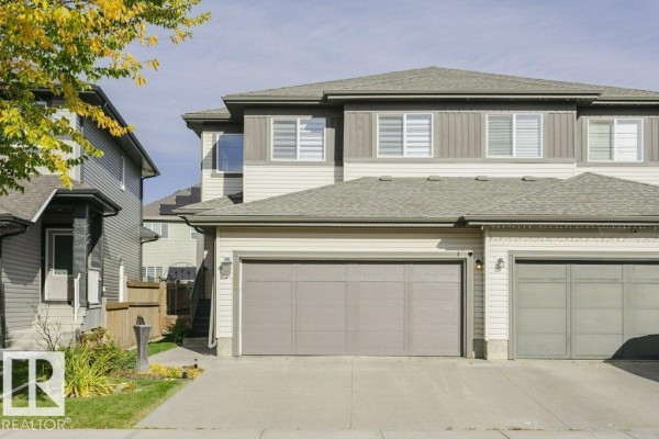 Exterior of a duplex featuring two grey garage doors and neutral siding. - 129 Harvest Ridge Dr, Spruce Grove