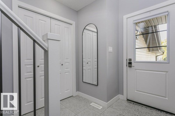 Interior entryway with grey walls, white bi-fold doors, a black arched mirror, and a white front door. - 129 Harvest Ridge Dr, Spruce Grove