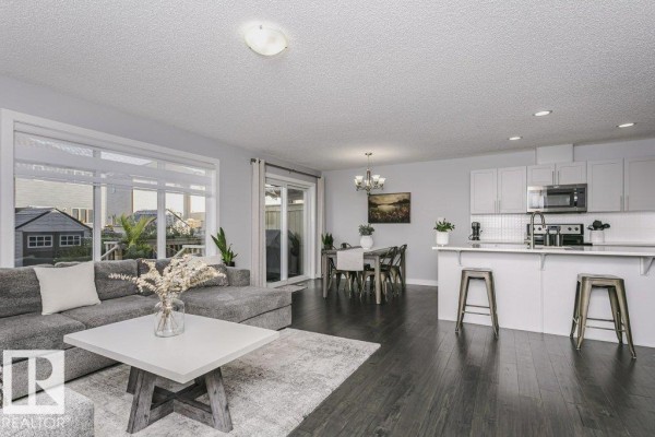 Open concept living and dining area with dark wood floors and white kitchen cabinets. - 129 Harvest Ridge Dr, Spruce Grove
