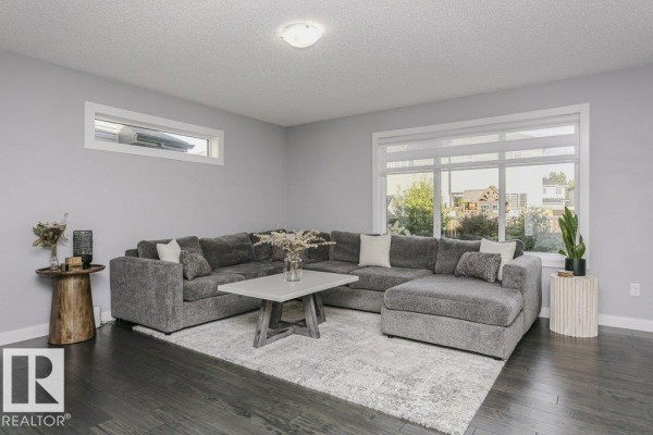 Spacious living room with a large sectional sofa, grey walls, and dark wood floors. - 129 Harvest Ridge Dr, Spruce Grove