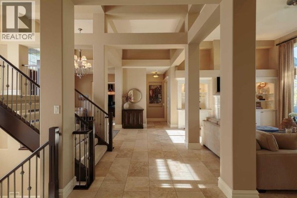 View down a wide hallway with beige walls and columns, showing a staircase, entryway, and access to other rooms. - 129 Heritage Lake Drive, Heritage Pointe