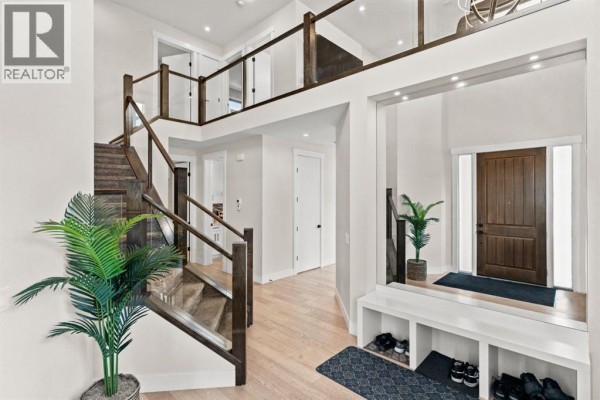 Bright, modern entryway with light wood floors, a dark wood staircase with glass railings, and a built-in bench with shoe storage. - 129 Marina Key, Chestermere