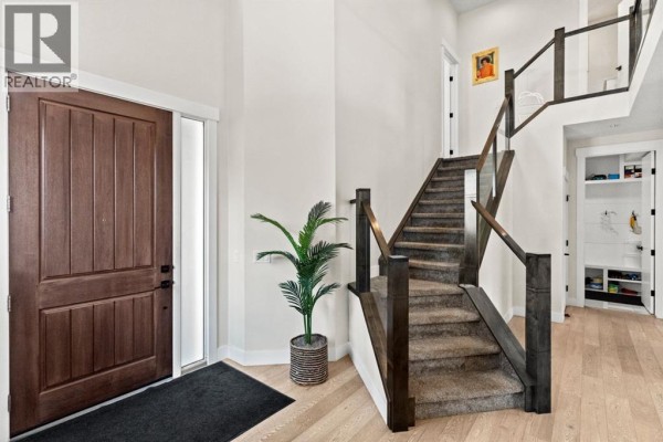 Close-up view of the dark wood front door and the carpeted staircase with dark wood banister and glass panels. - 129 Marina Key, Chestermere