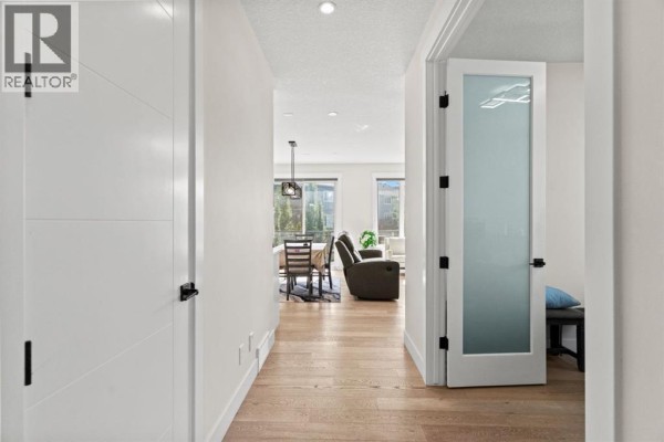 Hallway perspective looking towards an open-concept living and dining area with light wood floors and a frosted glass door. - 129 Marina Key, Chestermere