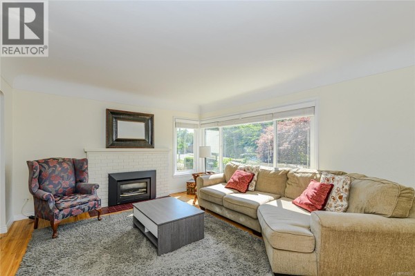 Living room with a sectional sofa, armchair, fireplace, and large windows with garden views. - 129 Moss St, Victoria