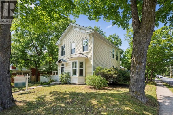 Side view of a yellow house showing the exterior siding, windows, and surrounding trees. - 129 Suffolk Street W, Guelph