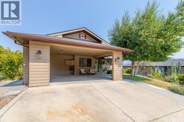 Carport with concrete floor and beige siding, connected to the house entrance. - 129 Sumac Ridge Drive, Summerland
