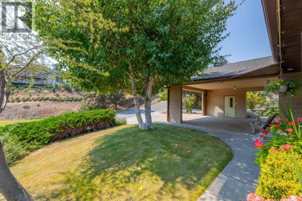 Pathway leading to a covered carport, with a green lawn and flowering plants. - 129 Sumac Ridge Drive, Summerland