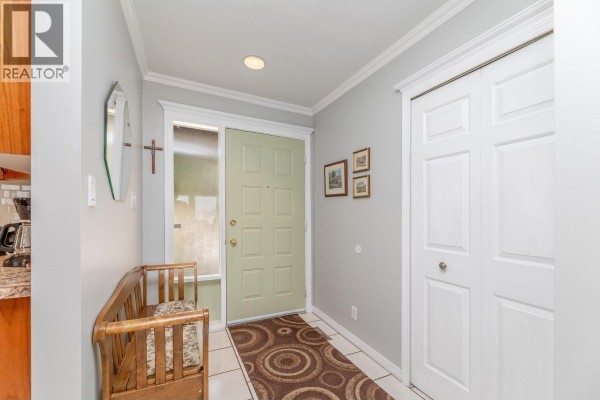 Interior entryway with a light green door, wooden bench, tiled floor, and white bi-fold closet doors. - 129 Sumac Ridge Drive, Summerland