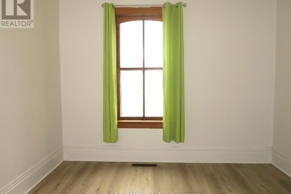 Room with light wood laminate flooring, white walls, and a wooden window with green curtains. - 129 Walnut Street, London North