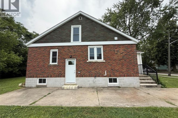 Rear view of a brick house with a white door, concrete patio, and green grass. - 1290 Laurendeau Avenue, Windsor