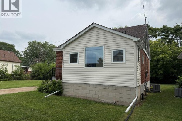 Side view of a brick and vinyl-sided house with large windows and air conditioning units outside. - 1290 Laurendeau Avenue, Windsor