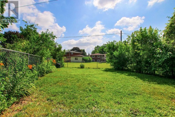 View of the backyard from the rear fence, showing a grassy lawn and neighboring houses. - 1292 Sorrel Road, London East