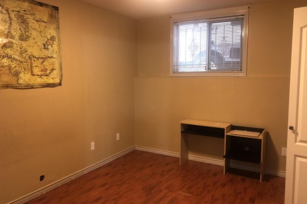 Room with yellow walls, wood floor, and a desk against the far wall. - 12930 109 Avenue, Surrey