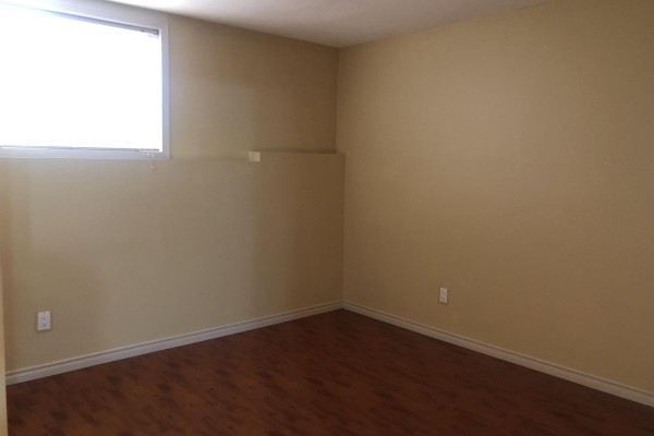 Empty room with beige walls, wood floor, and a window with blinds. - 12930 109 Avenue, Surrey