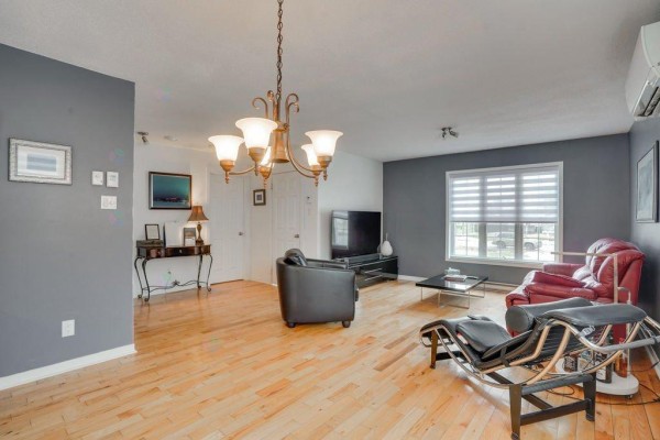 Living room with grey walls, light wood floors, red leather sofa, and black armchair. - 1294 Rue D'alma, Gatineau