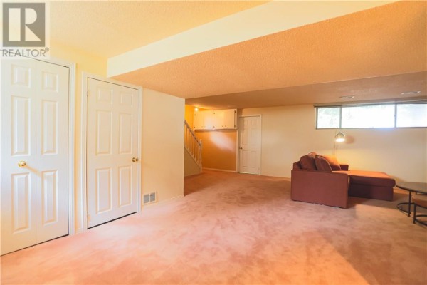 Finished basement living room with peach carpet, beige walls, white doors, and red sofa - 1295 Gemmell Street Sudbury