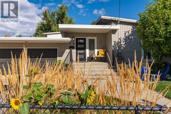 Front entrance of a duplex with a modern black door and yellow chair. - 1296 Kelglen Crescent, Kelowna