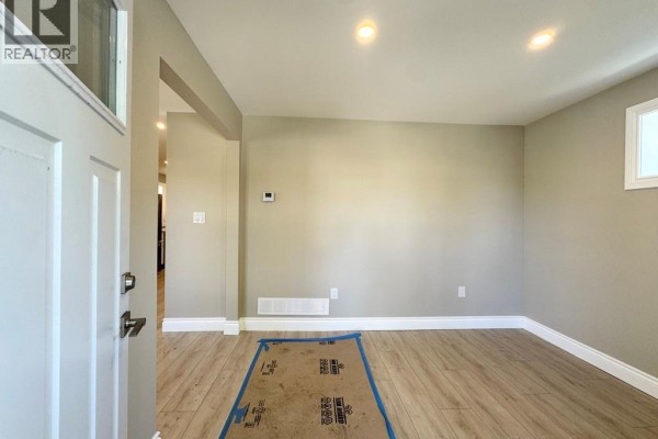 Interior view of a room with beige walls, light wood laminate flooring, and a covered floor area. - 1296 Laurendeau Avenue, Windsor