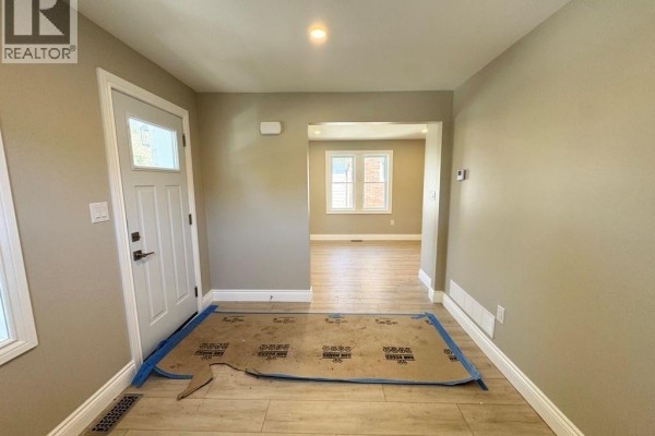 Entrance area with a white door, light wood flooring, and an open doorway to another room. - 1296 Laurendeau Avenue, Windsor
