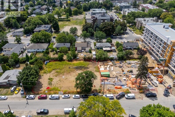 View of the lot from across the street, showing adjacent homes, construction activity, and a new building. - 1299-1329 Pridham Avenue, Kelowna