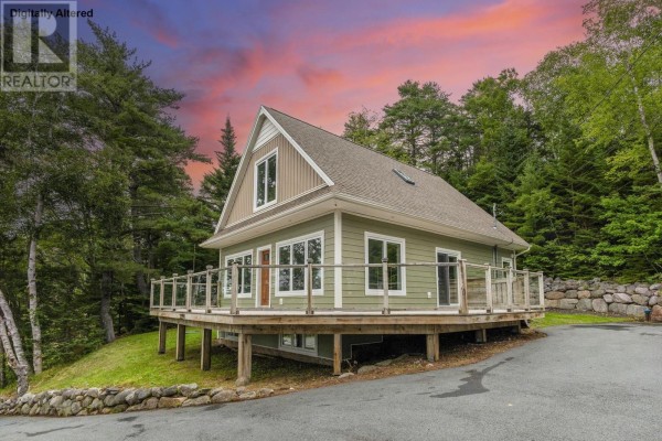 Side view of a green house with a wooden deck and surrounding trees under a colorful sunset sky. - 12991 Peggys Cove Road, Tantallon