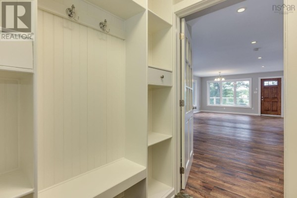 Entryway with white built-in shelving, beadboard walls, and a view into a living room with wood floors. - 12991 Peggys Cove Road, Tantallon