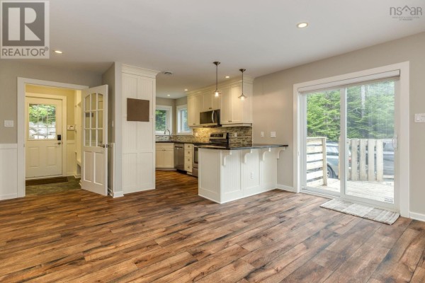 Open-concept living space with a kitchen, island, dining area, and sliding glass doors to a deck. - 12991 Peggys Cove Road, Tantallon