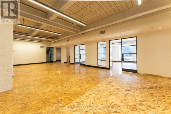 Wide view of the commercial space, featuring OSB flooring, white brick pillars, and glass doors. - 12a - 219 Dufferin Street, Toronto