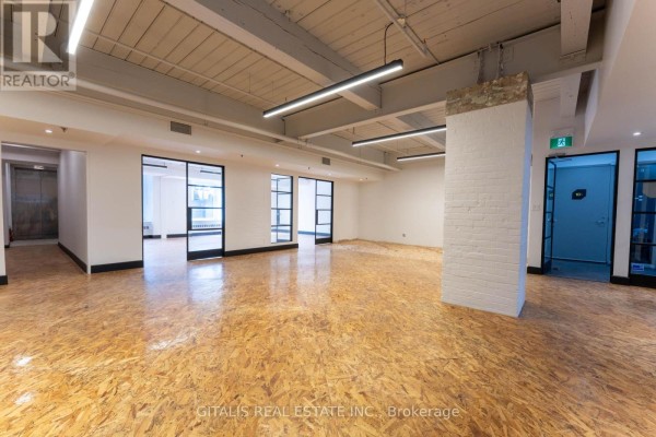 Commercial space showing an elevator bank, white brick pillars, OSB flooring, and glass doors. - 12a - 219 Dufferin Street, Toronto